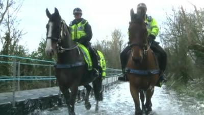 Police officers on horses in flood water