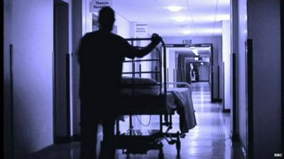 Outline of man pushing empty hospital trolley down corridor