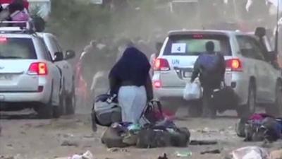 Woman carrying bags out of Homs