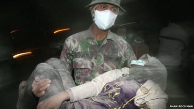 An Indonesian military soldier carries a collapsed resident during the evacuation following eruption of Mount Kelud