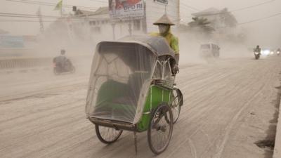 A man wears a mask as he rides a becak