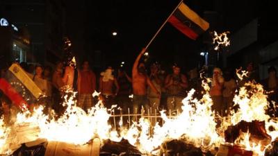 Opposition demonstrators hold a Venezuelan flag in front of a burning barricade in Caracas