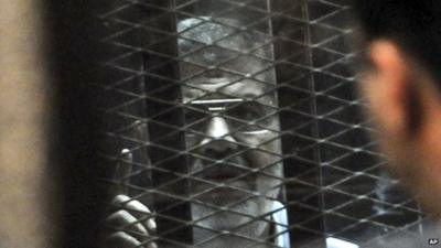 Mohammed Morsi speaks from a glassed-in defendant's cage during his trial over charges related to prison breaks