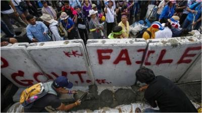 Anti-government protesters pour cement near a concrete wall set up to block a gate of the Government House during a rally in Bangkok