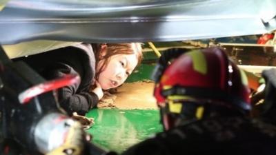 A woman trapped in the rubble of a collapsed resort building, waits to be rescued