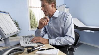 Doctor in his surgery room checking notes at his computer