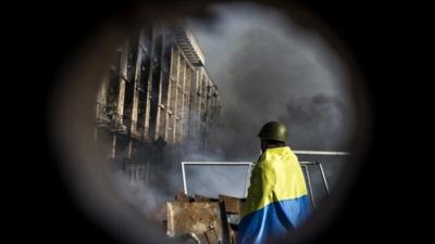 An anti-government protester wrapped in the Ukrainian national flag stands by a barricade during clashes with riot police on Kiev's Independence square on February 19, 2014