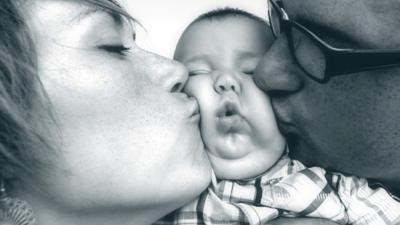 Mother and father kissing baby on both cheeks