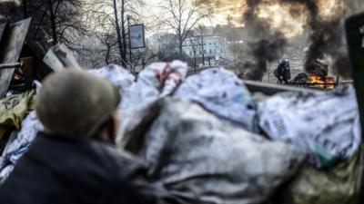 An anti-government protestor looks at a protestor adding tires to a fire at a barricade