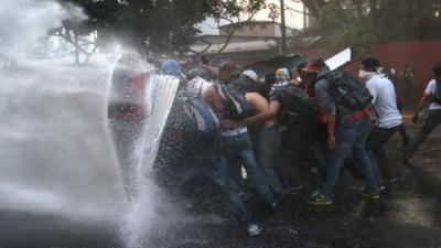 Protesters hold a barricade against a water canon fired by the Venezuelan national guard during an anti-government demonstration on February 27, 2014 in Caracas