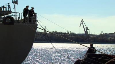 Sailors on board a ship talk to a man on land