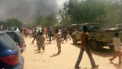 People walk in a street as smoke rises after Boko Haram Islamists attacked a military base in the northeast Nigerian city of Maiduguri on March 14, 2014