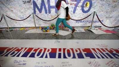 A woman walks past a banner filled with messages of hope for the missing Malaysia Airlines jetliner MH370 at Kuala Lumpur International Airport