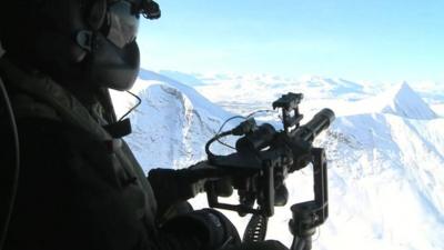 Soldier aiming gun out of helicopter in arctic