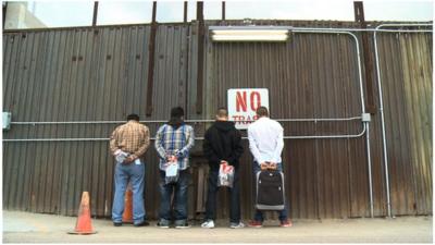 Immigrants about to be deported from US to Mexico line up against the border fence