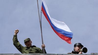 A man holds a Russian flag on the roof of the naval headquarters in Sevastopol