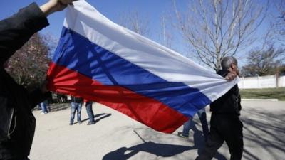 Two men carry a Russian flag after storming the base in Novofedorivka