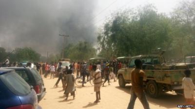 People walk in a street as smoke rises after Boko Haram Islamists attacked a military base in the northeast Nigerian city of Maiduguri on March 14, 2014