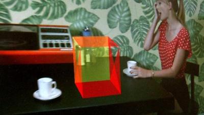 A woman sitting next to a computer generated box on a table