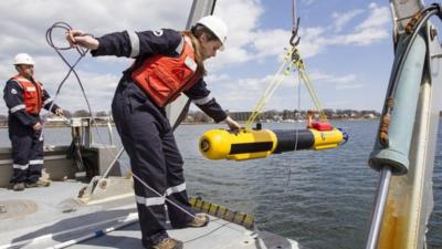 A submarine built by Bluefin Robotics is lowered into the water by systems engineer Cheryl Mierzwa in Quincy