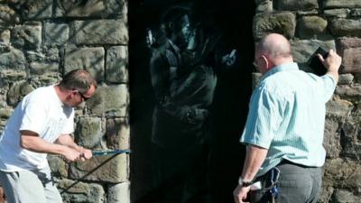 The Banksy being removed by two men