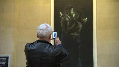 Man takes photo on phone of Banksy art