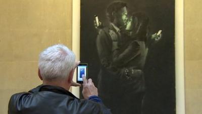 Man takes photo on phone of Banksy art