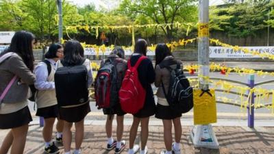 School children hang yellow ribbons by a road side at the main gate of Danwon high school