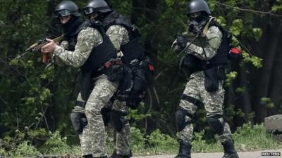 Ukrainian security force officers walk past a checkpoint set on fire and left by pro-Russian separatists near Sloviansk