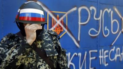 A pro-Russian militant adjusts his mask in Sloviansk , eastern Ukraine- slogan reads 'Russia do not surrender'