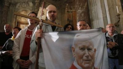 Polish pilgrims hold a flag portraying Pope John Paul II during a vigil prayer