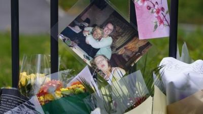 A photograph of teacher Ann Maguire (L) who was fatally stabbed sits with floral tributes outside Corpus Christi Catholic College in Leeds