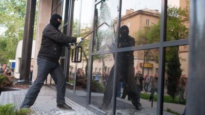 A pro-Russian activist breaks the glass of offices of the Industrial Union of Donbass Corporation in Donetsk