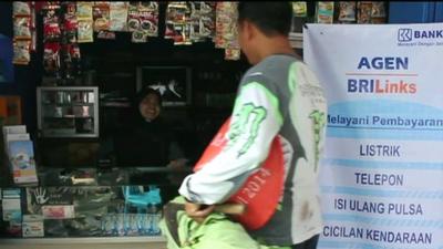 A farmer withdraws money from a bank agent at a local shop in central Java