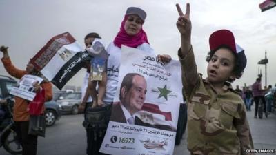 An Egyptian boy dressed in army clothes flashes the sign for victory as his mother holds a poster bearing an image of presidential candidate Abdul Fattah al-Sisi during a rally in Cairo, 20 May 2014