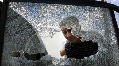 A local looks at a damaged vehicle following a gun battle