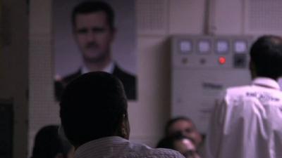 Men's backs with poster of President Assad in background