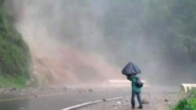 A man holds an umbrella as water cascades onto a road in Guatemala