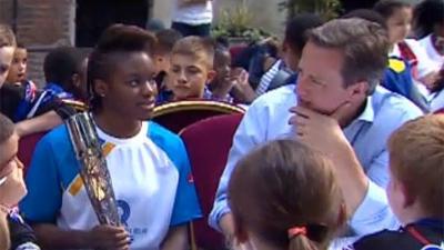 David Cameron talks to a young athlete who is holding the Queen's Baton.