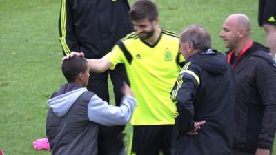 Spain defender Gerard Pique hands his tracksuit top to a young fan