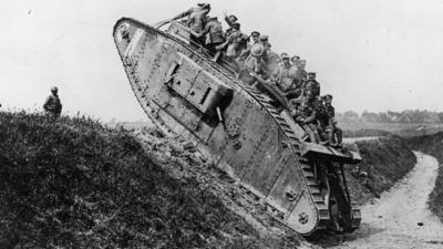 British troops riding on the back of the Mark IV tank as it crawls over a trench ledge in 1918