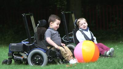 Two boys playing with an inflatable football in their chairs, which are low to the ground so they can kick it