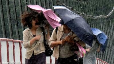 Pedestrians with umbrellas are battered by a storm