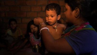 A young mother spoons oral rehydration therapy into a boy's mouth