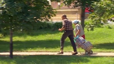 elderly couple run along path with bags on trolley