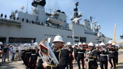 The band of The Royal Marines perform next to HMS Illustrious as she sails into her home port of Portsmouth for the final time ahead of being retired next month