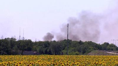 Smoke rises on the outskirts of Donetsk over sunflower field