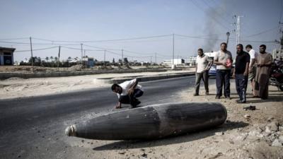 A Palestinian man inspects an Israeli warhead that failed to explode on the side of a road, during a ceasefire in Deir al-Balah, central Gaza Strip