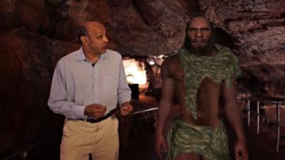 Pallab Ghosh walking next to simulation of a Neanderthal man