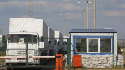 A Russian aid convoy of white trucks waits to enter Ukraine at a border control point